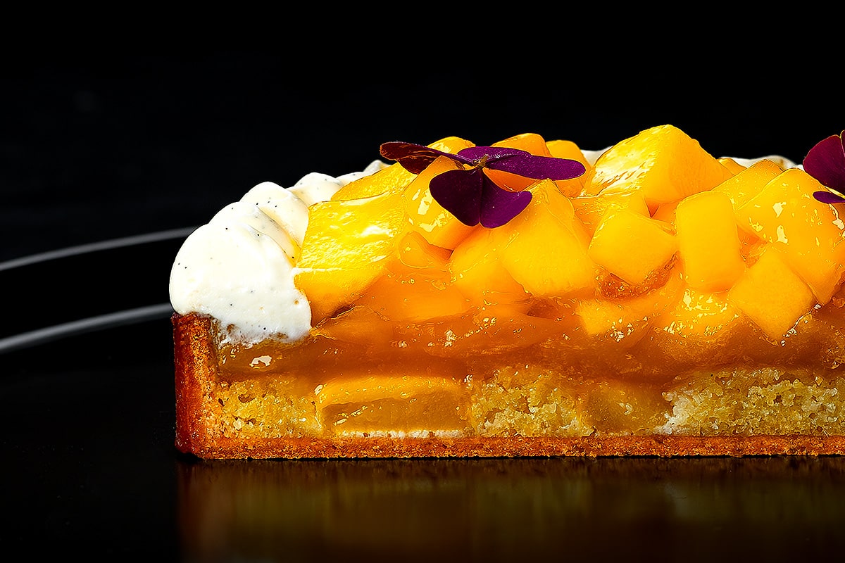 découpe de tarte mangue vanille sur fond noir