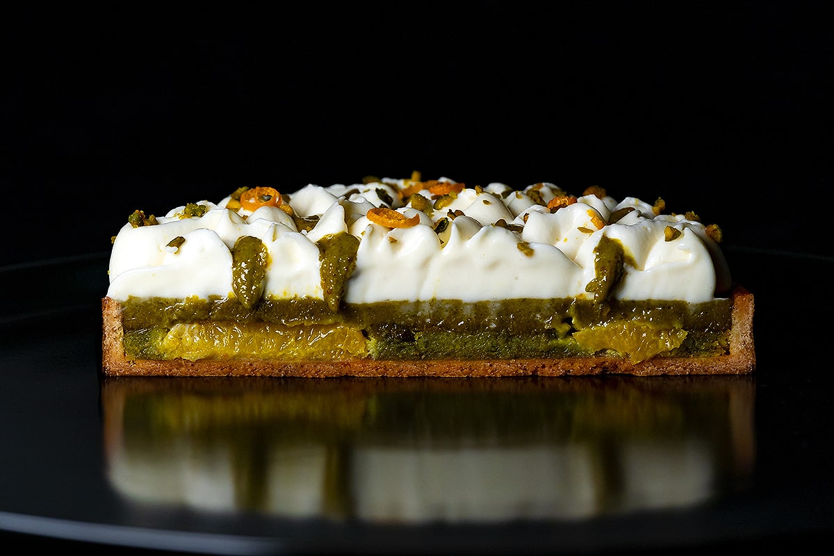 découpe de la tarte à la pistache et fleur d'oranger sur fond noir